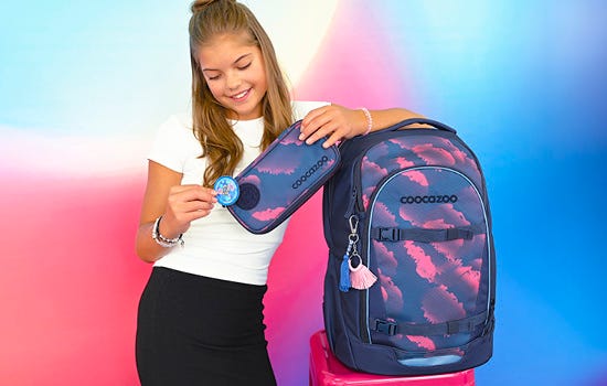 For your EVERYday Ein Mädchen lehnt an ihrem EVERY Rucksack mit lachendem Blick auf ihr Mäppchen